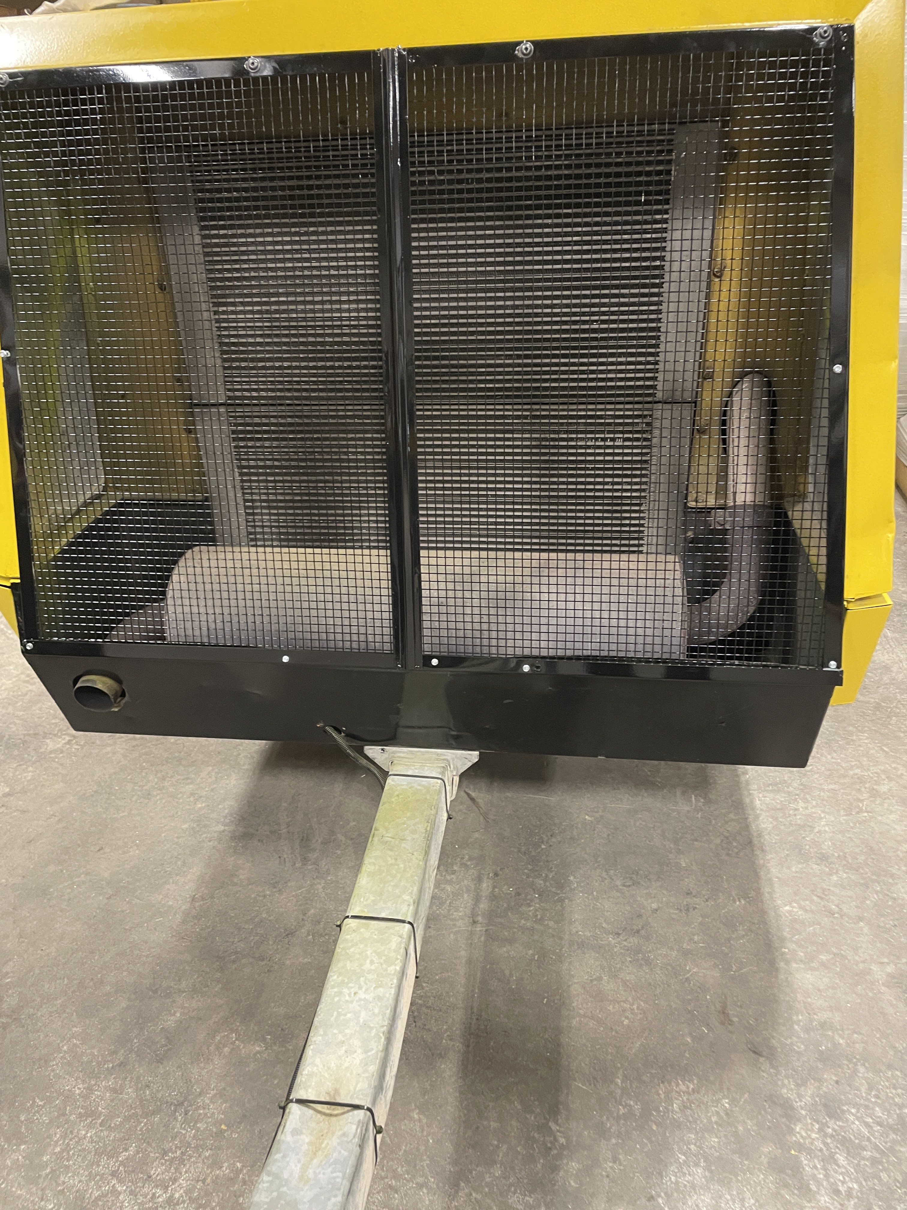 Close-up view of a yellow industrial machine with a black mesh grill and a metal tow bar extending towards the camera, on a concrete floor.
