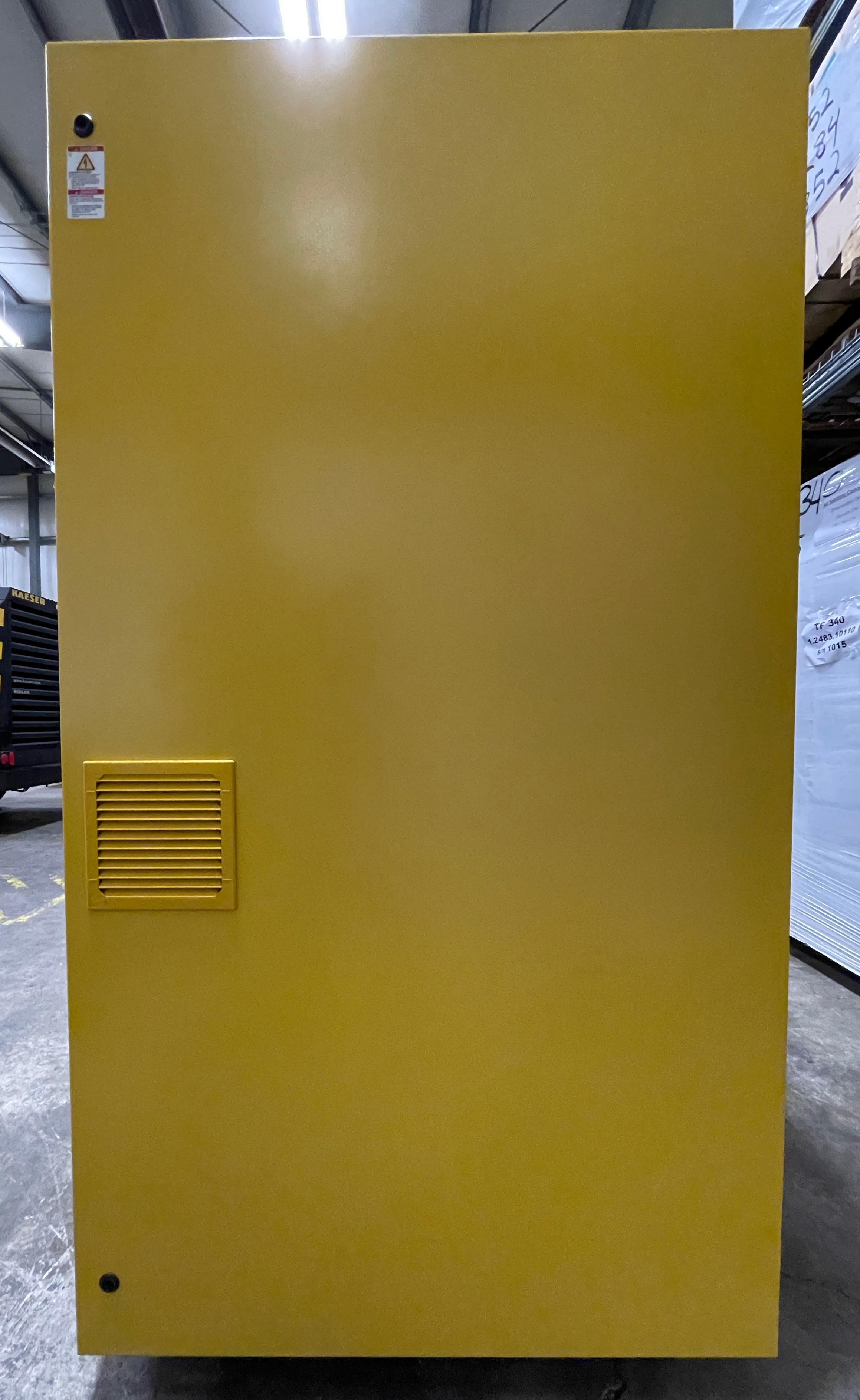 A large, vertical, yellow industrial cabinet with a vent and a caution sticker is situated in a warehouse environment.