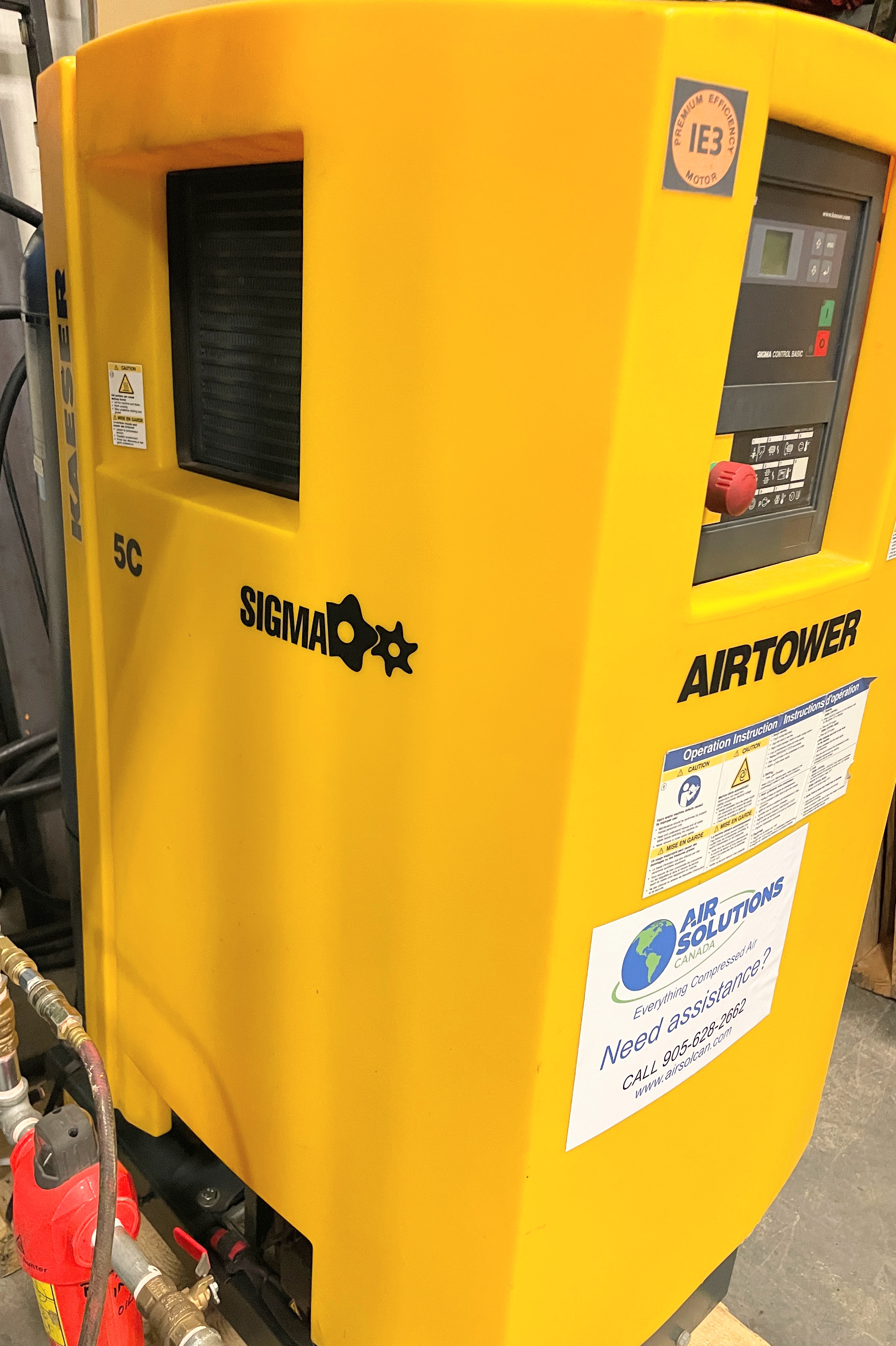 Yellow KAESER AIRTOWER SIGMA 5C industrial air compressor with control panel and service information label, installed indoors near red piping.