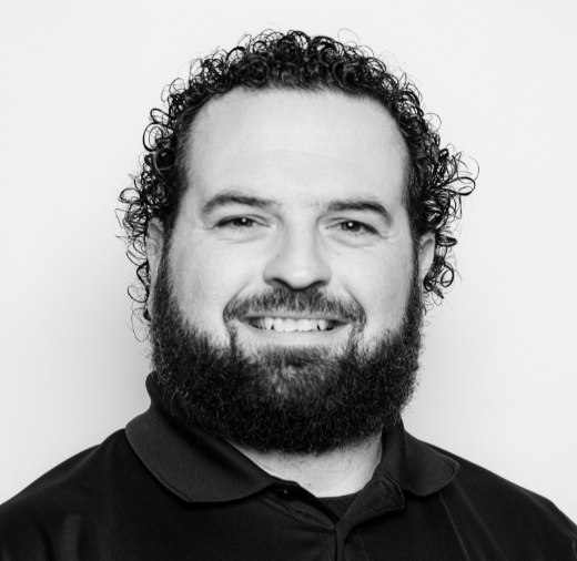 Black and white photo of a person with curly hair and a beard, smiling at the camera.