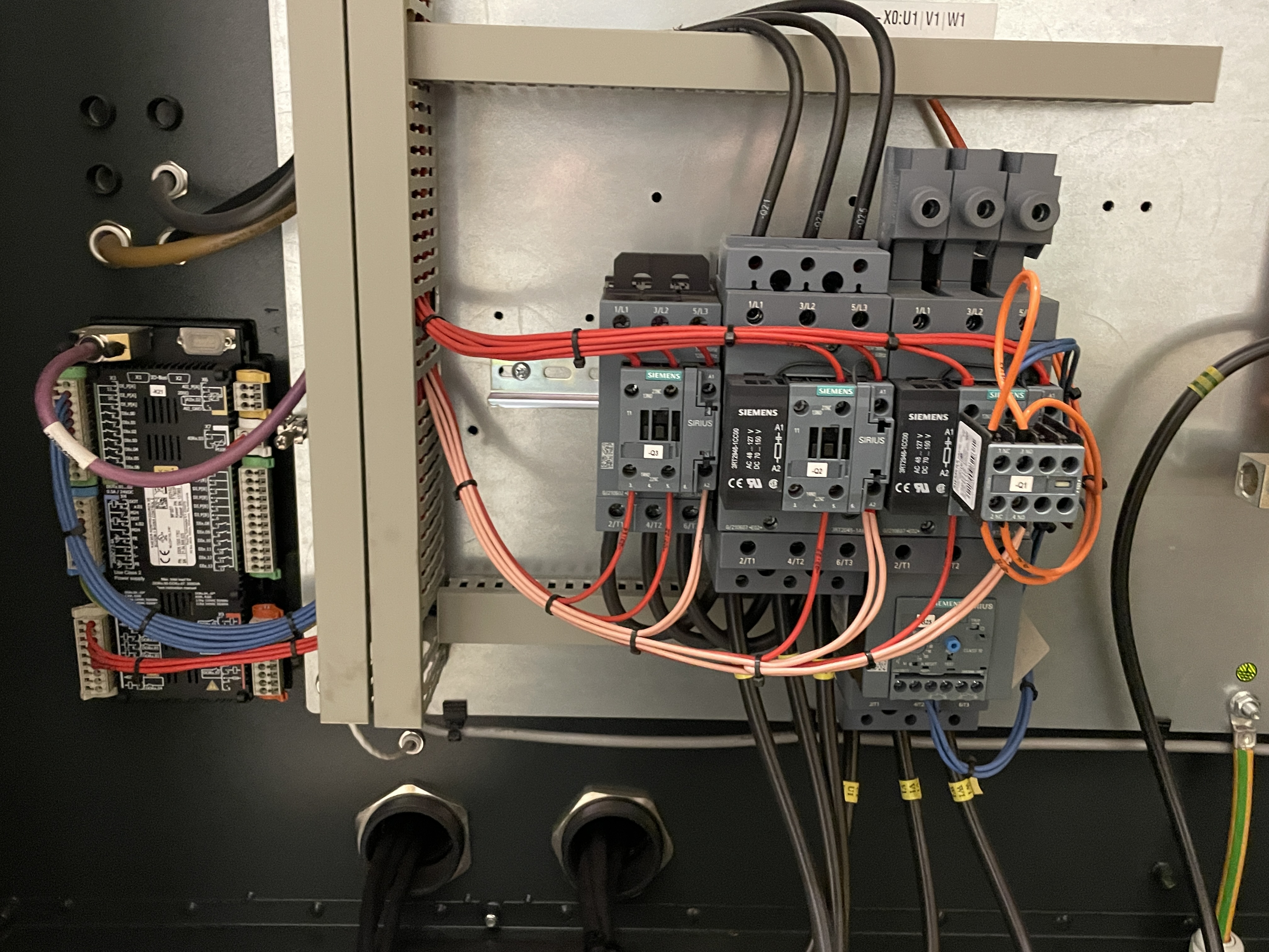 Close-up of electrical components and wiring inside an industrial control panel, including circuit breakers, relays, and multiple cables connected to different terminals.