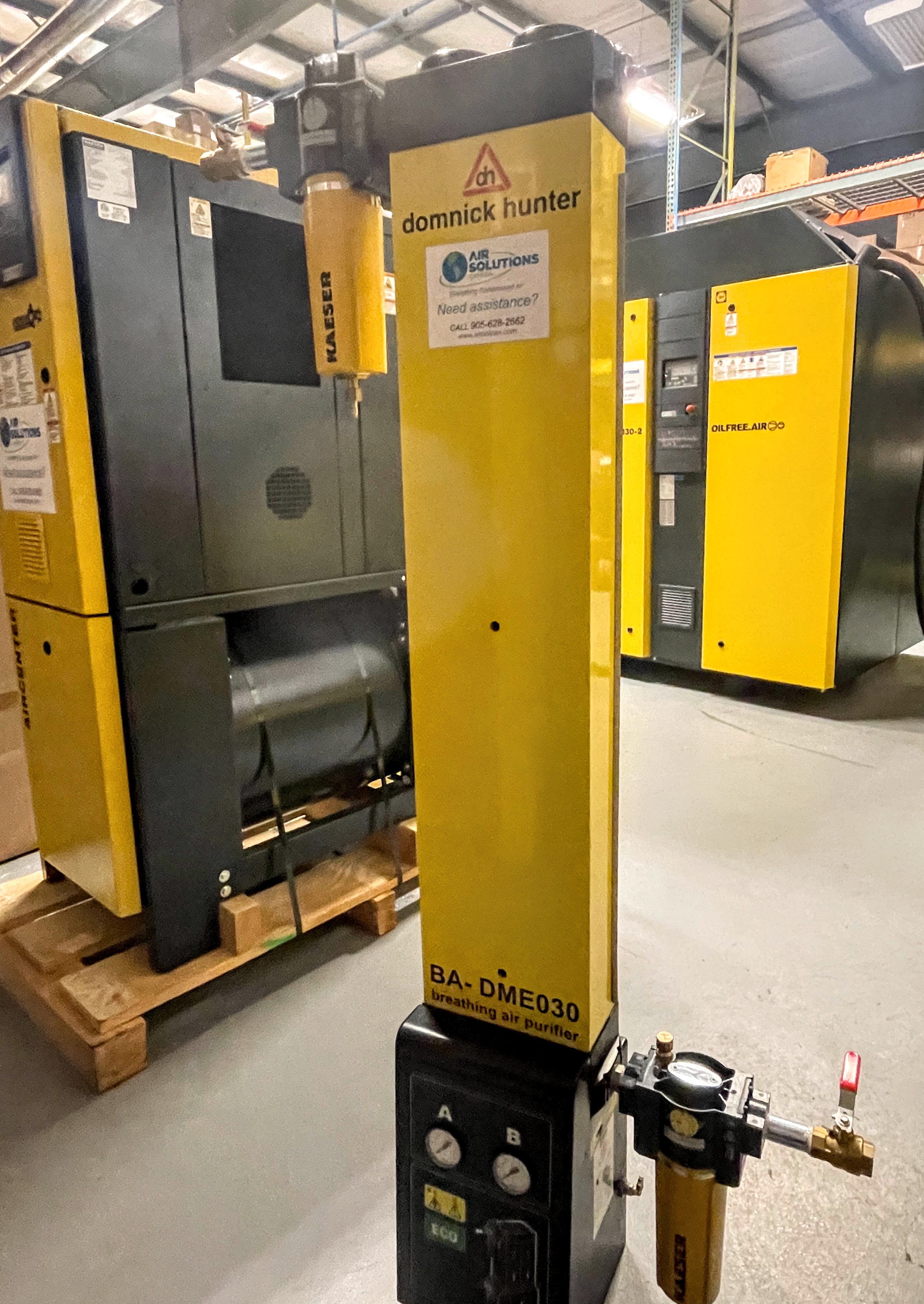 A yellow domnick hunter BA-DME030 breathing air purifier stands in an industrial warehouse, surrounded by other large yellow and black equipment.