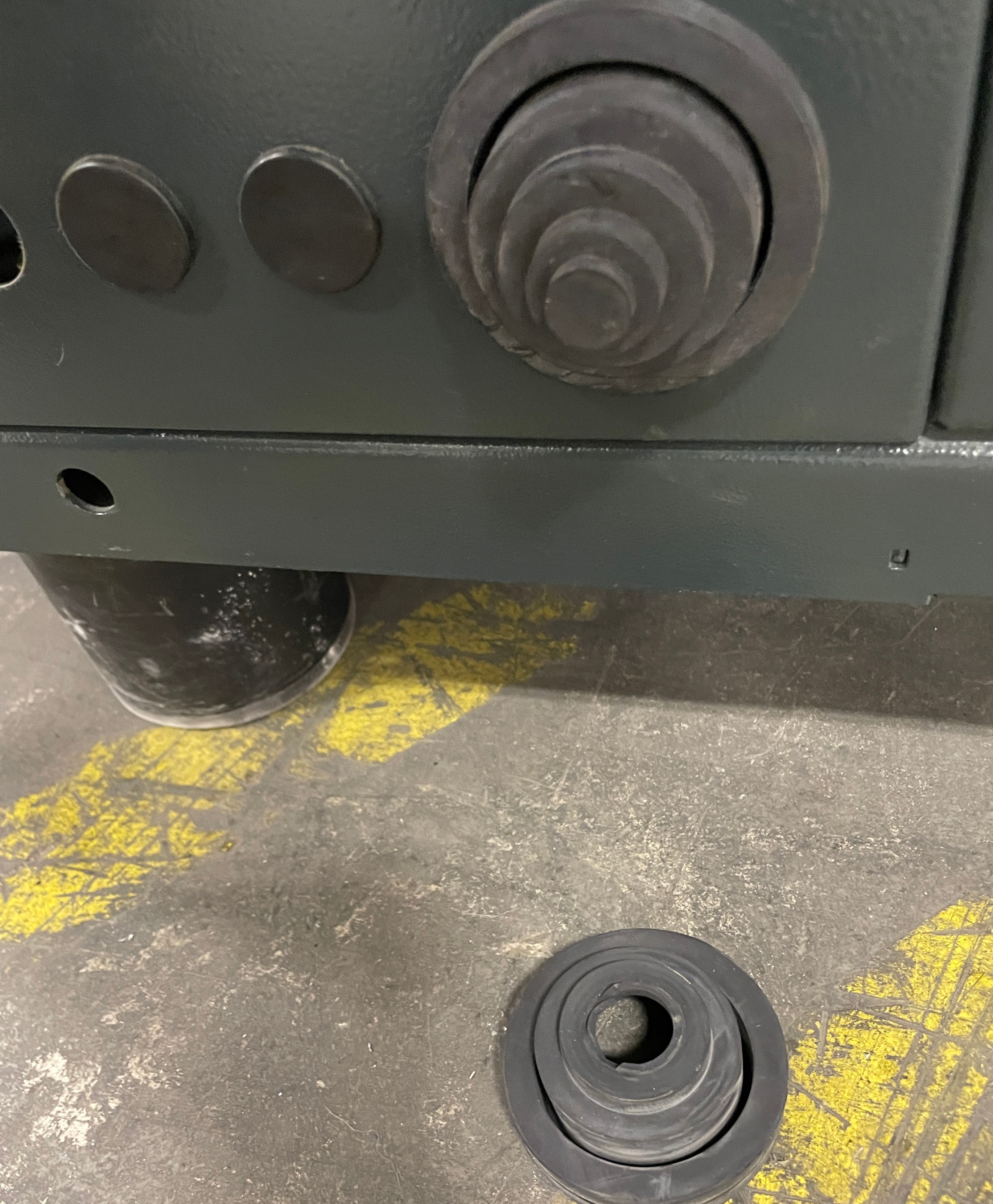 A coiled spring object next to a similar object attached to a metal machine panel on a concrete floor with partial yellow markings.