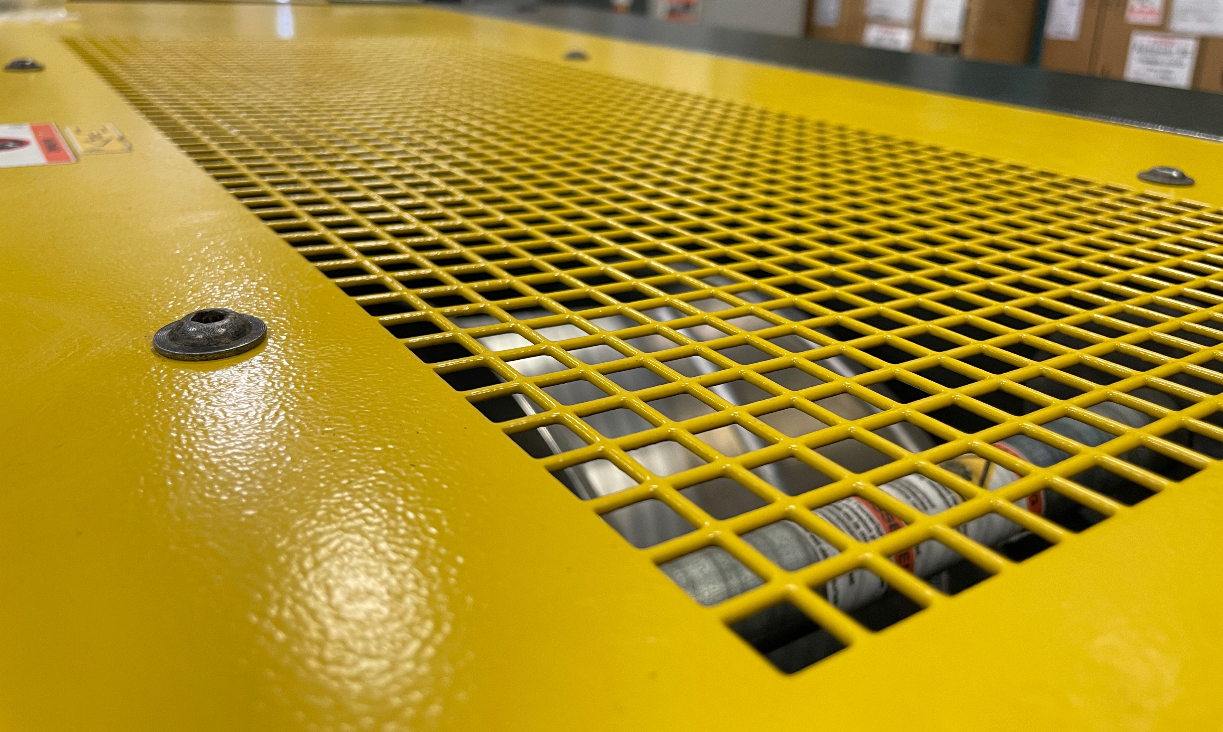 Close-up view of a yellow industrial machine with a grated metal cover, revealing some internal components.