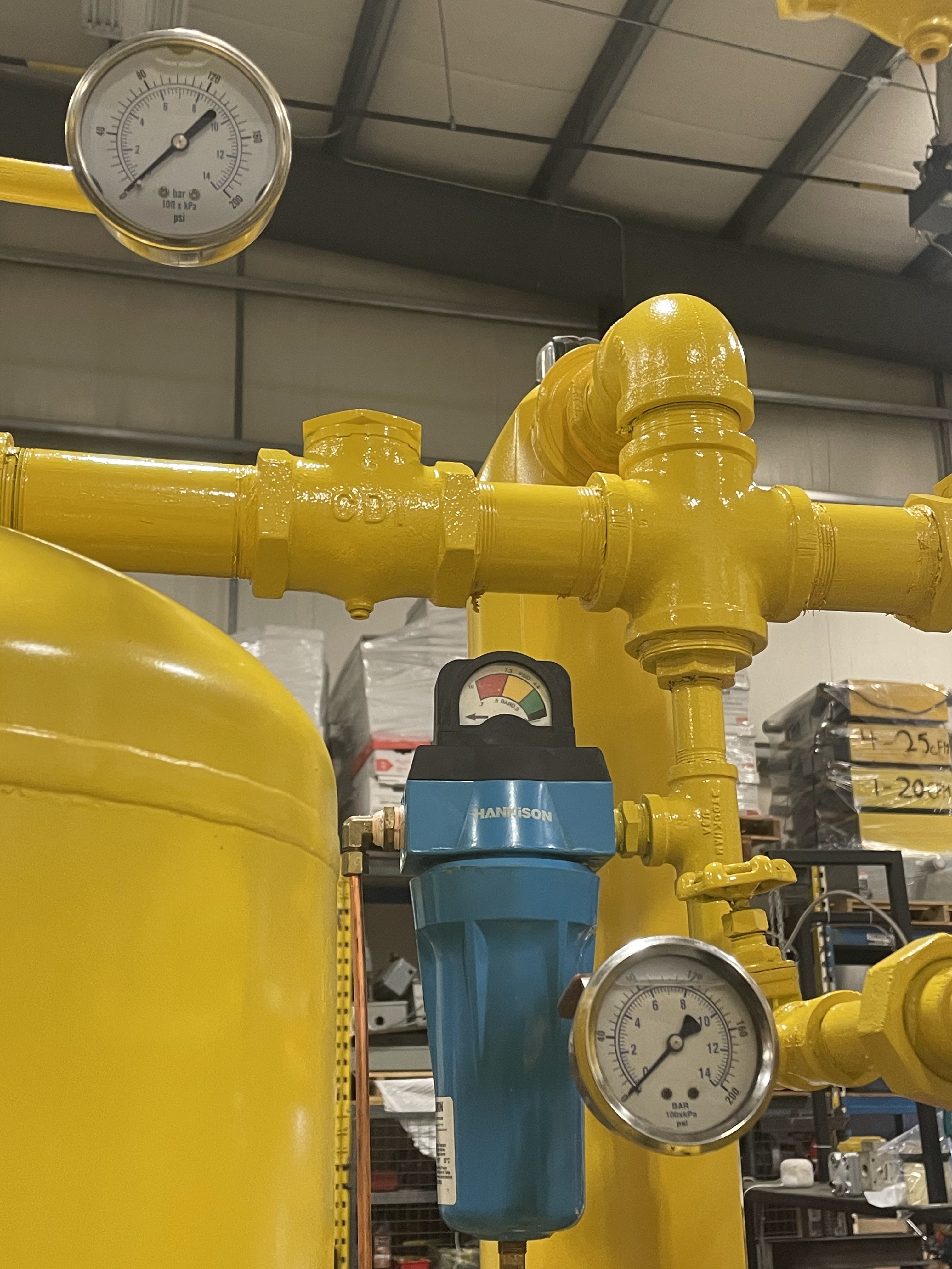 Yellow industrial pipes with pressure gauges and a blue Harrison branded filter in a warehouse setting.