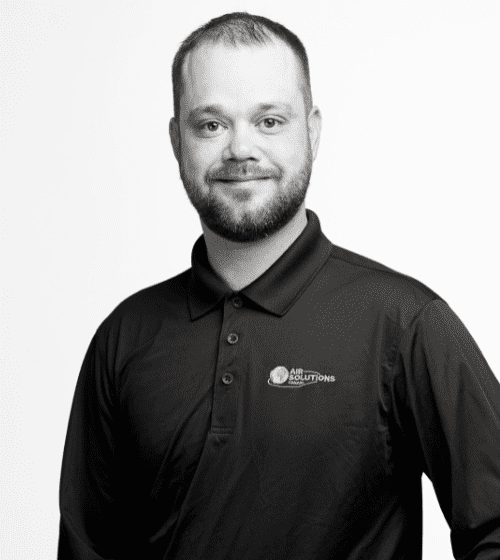 A man with short hair and a beard is wearing a black polo shirt with the Air Solutions logo on it. He is standing against a plain white background and looking at the camera.