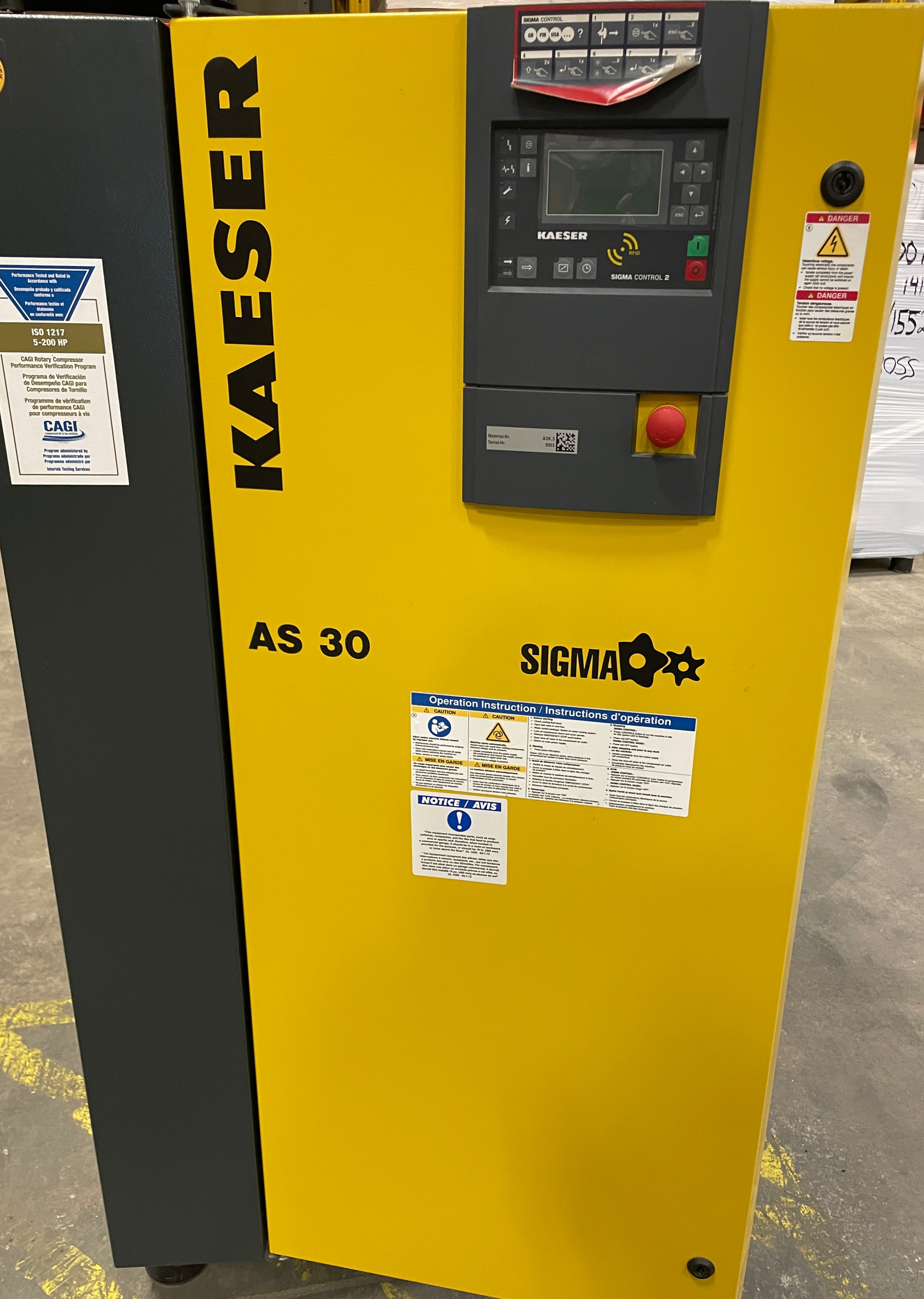 A yellow and black Kaeser AS 30 Sigma air compressor with a control panel and visible warning labels, standing on a gray floor.