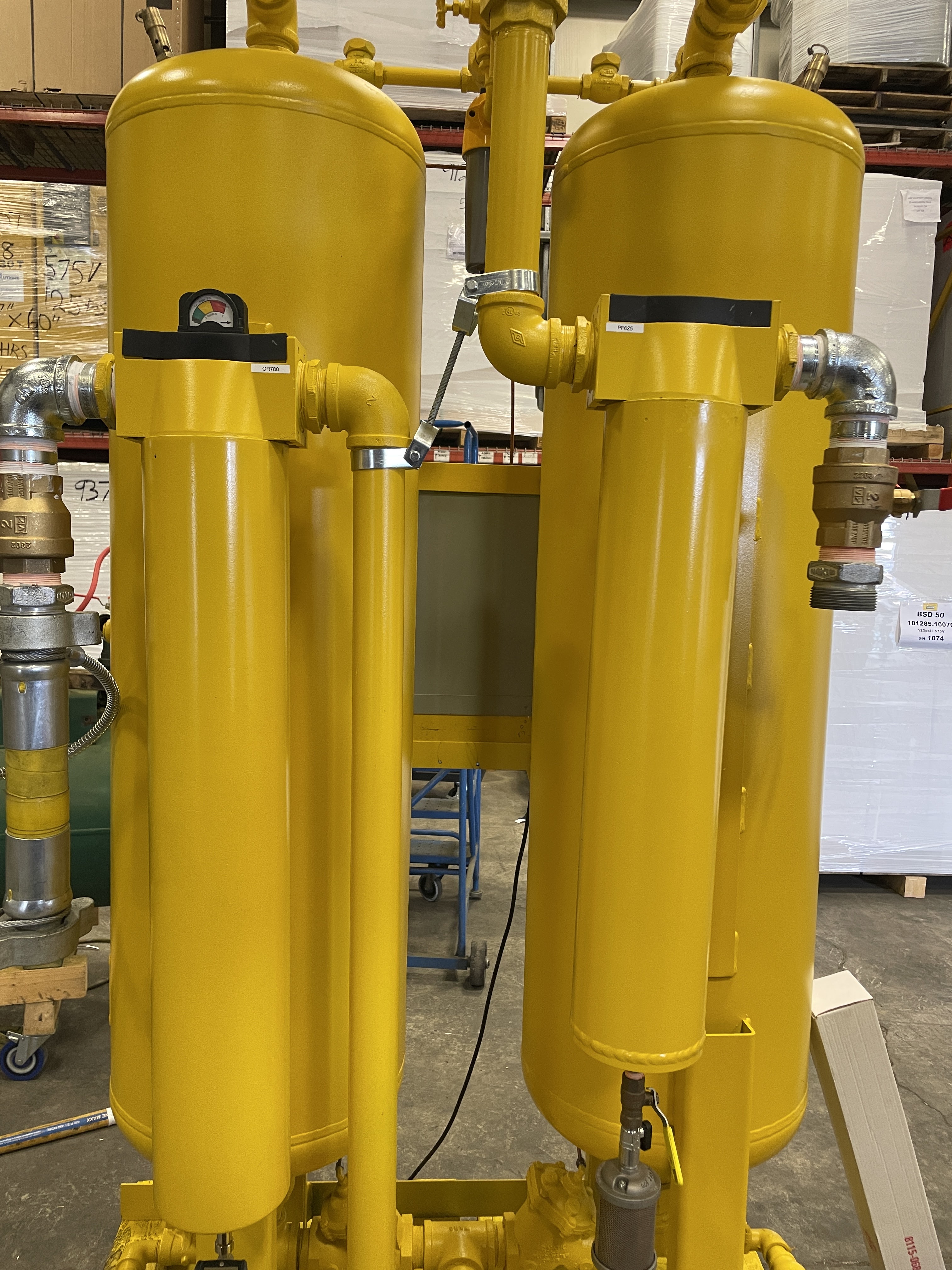 Two large, vertical yellow industrial tanks with attached pipes and gauges in a warehouse setting.