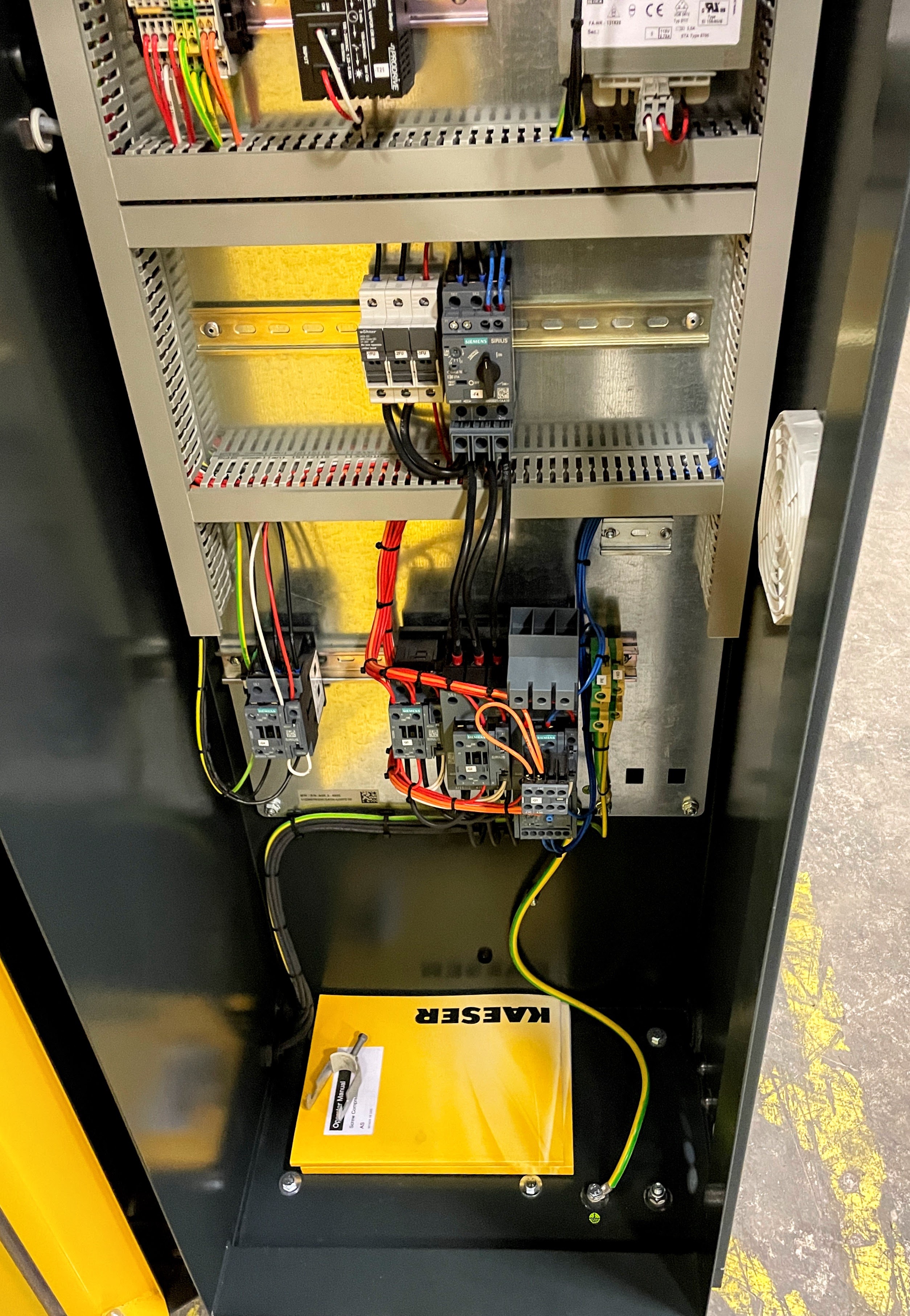 Electrical control panel with various wires, switches, and components. A yellow manual labeled "KÄSER" is placed at the bottom.