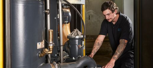 A technician with tattoos inspects industrial machinery in a workshop.